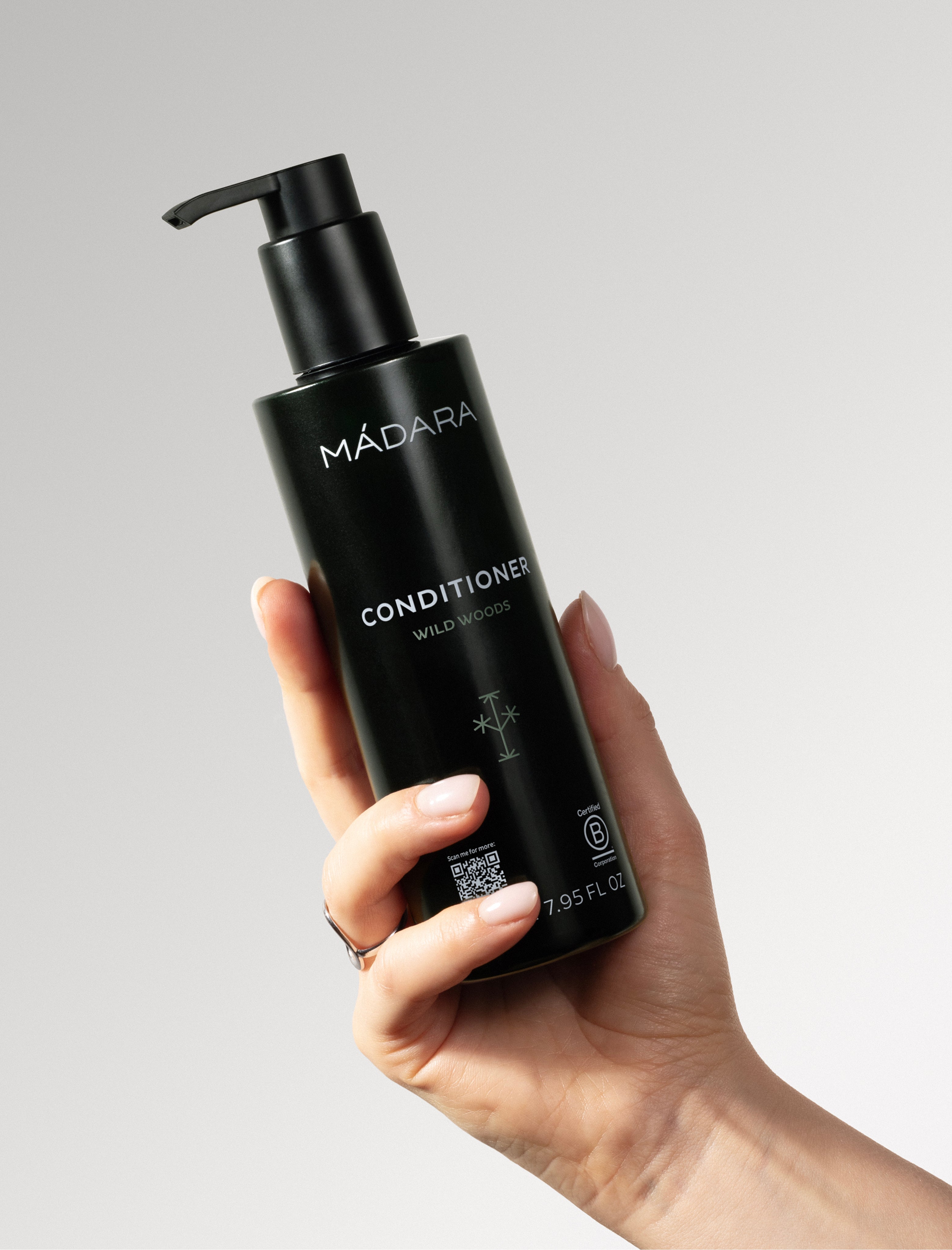 Hand holding a black Mádara conditioner bottle against a gray background
