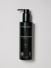 Black bottle of Mádara Wild Woods conditioner on a light gray background
