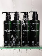 Set of Madara skincare products including Hand & Body Wash, Body Lotion, Shampoo, and Conditioner on a glass shelf with water droplets.
