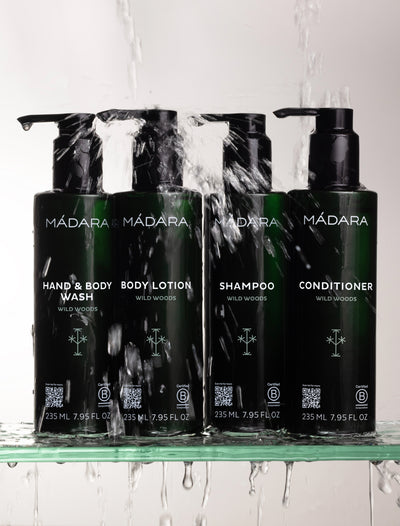 Set of Madara skincare products including Hand & Body Wash, Body Lotion, Shampoo, and Conditioner on a glass shelf with water droplets.