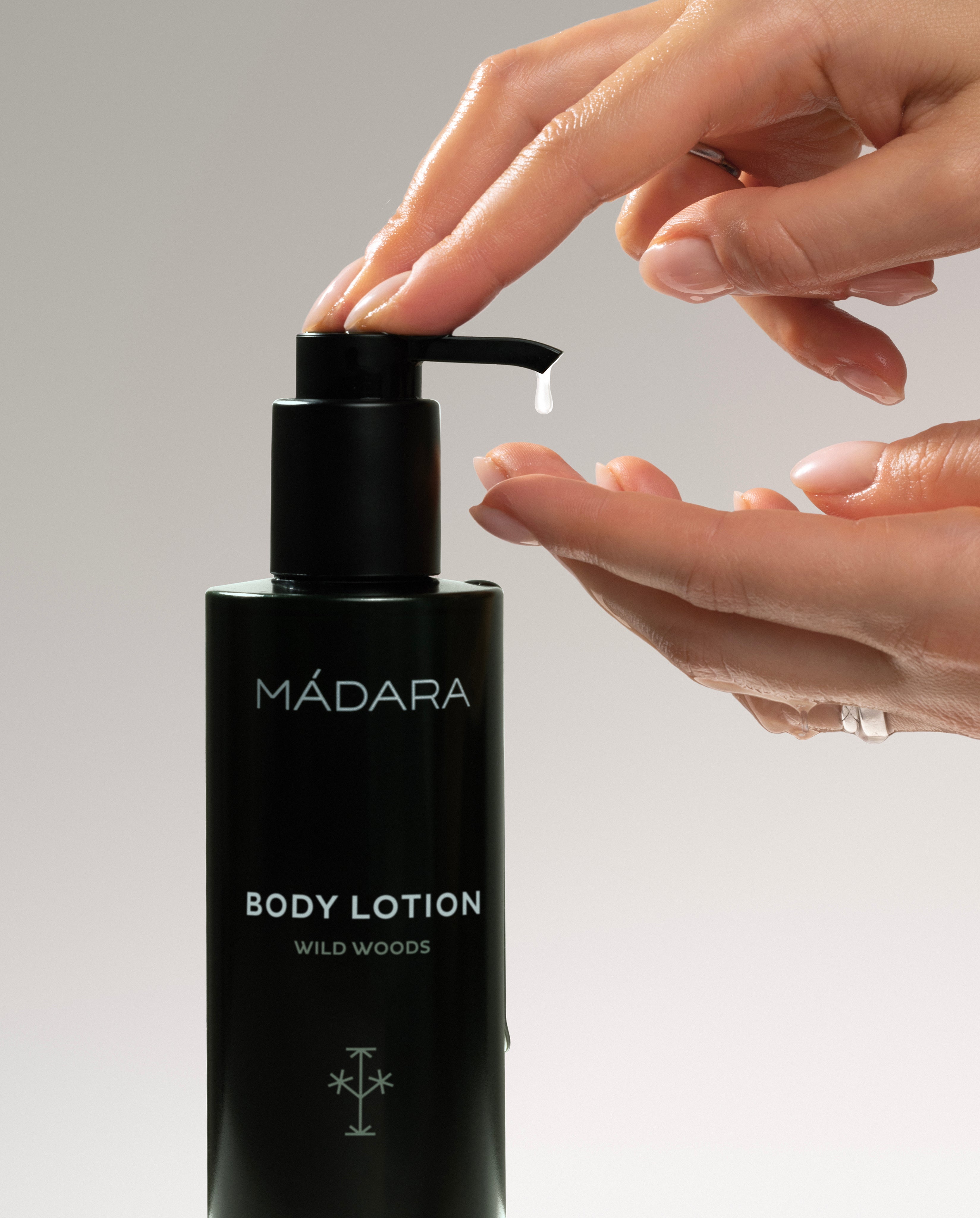 Black body lotion bottle with pump being used, featuring the brand 'Mádara'.
