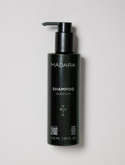 Black shampoo bottle with pump labeled 'Mádara' on a light gray background