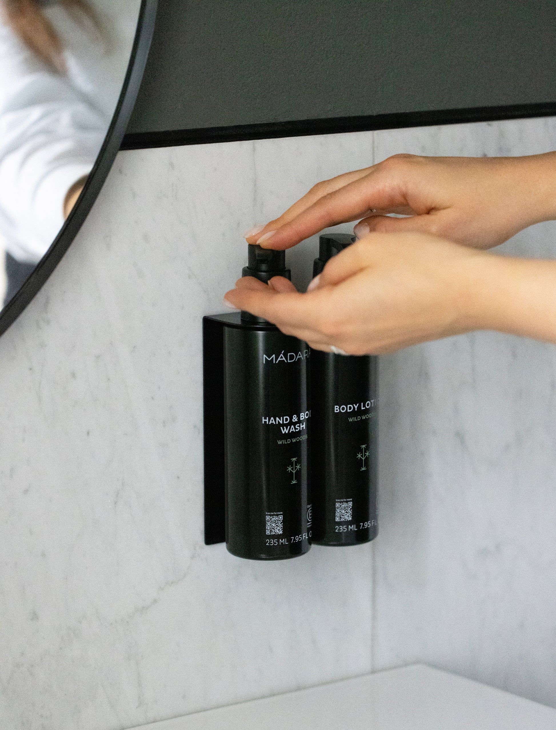 Person using a black soap dispenser on a marble wall