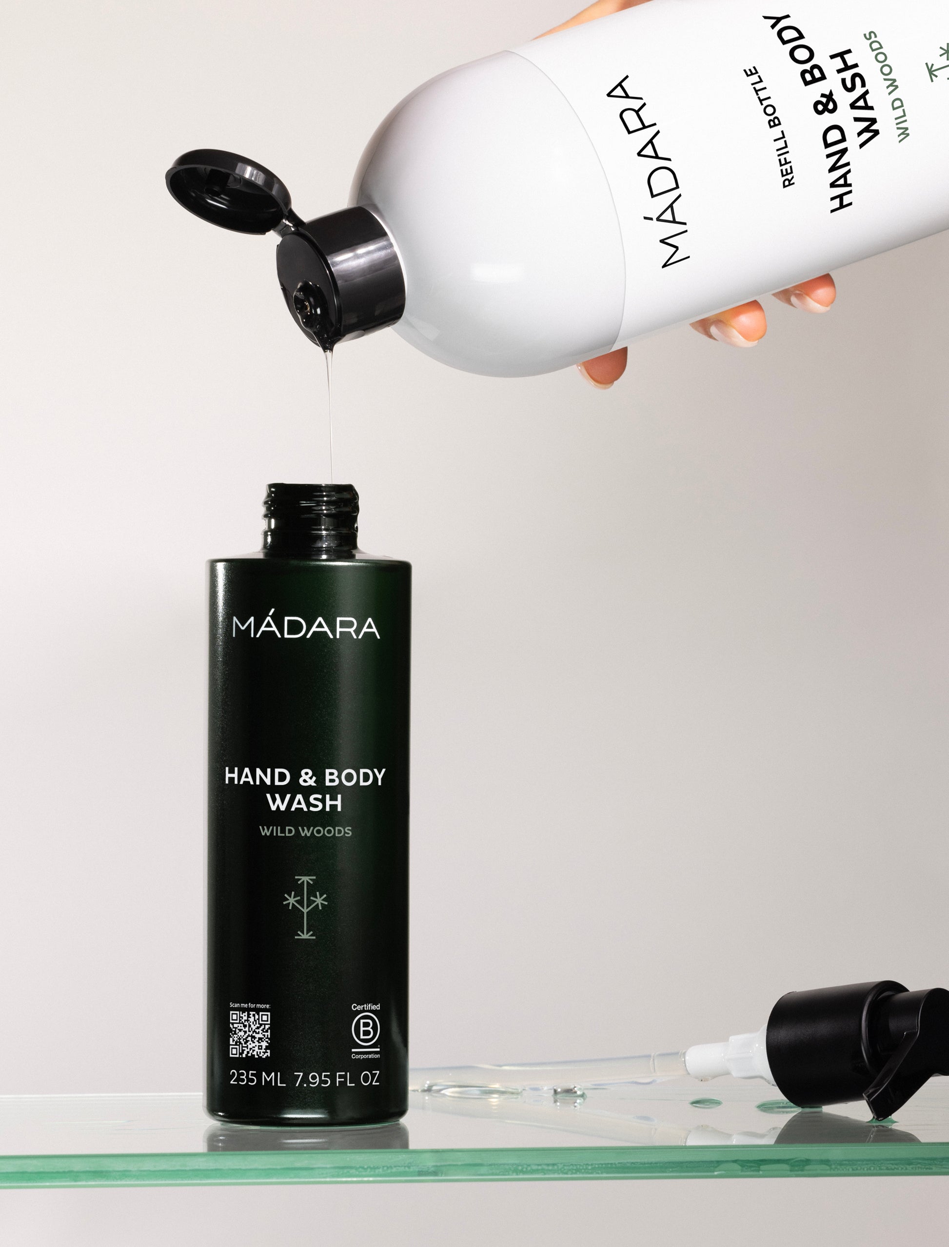 Mádara hand and body wash being poured from a refill bottle onto a black bottle.
